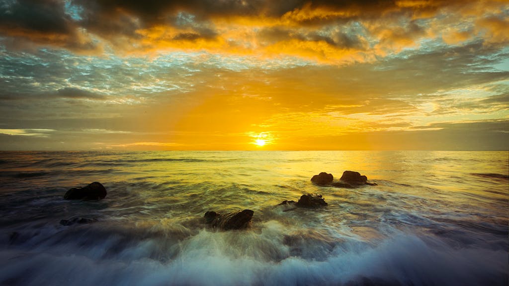 Dramatic sunrise over ocean waves with rocks on the shore, captured vividly.